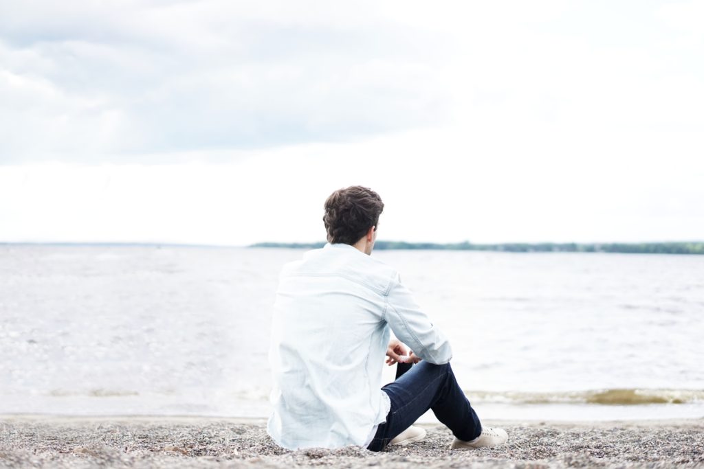 Young man relaxing as he stares across the water, relieved.